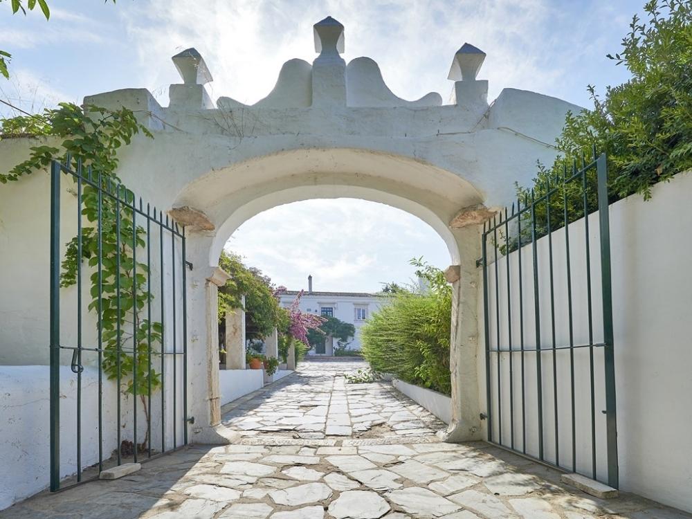 Weingut Quinta do Mouro in Portugal. Blick auf den Eingang des Weingutes, eine weiße Mauer mit Tor, gepflasterter Weg.