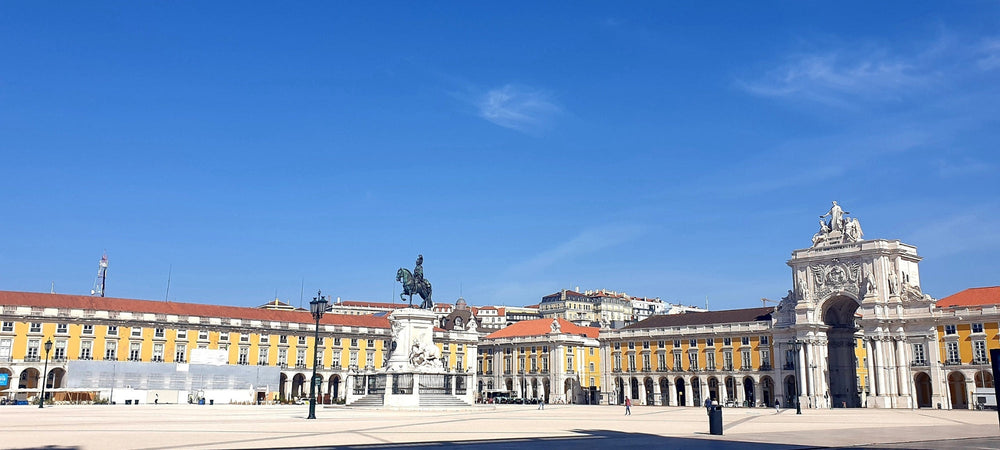 Ein sonniger Tag auf dem Praça do Comércio in Lissabon. Kopfsteinpflaster, gelbe Gebäude und der Triumphbogen Arco da Rua Augusta.