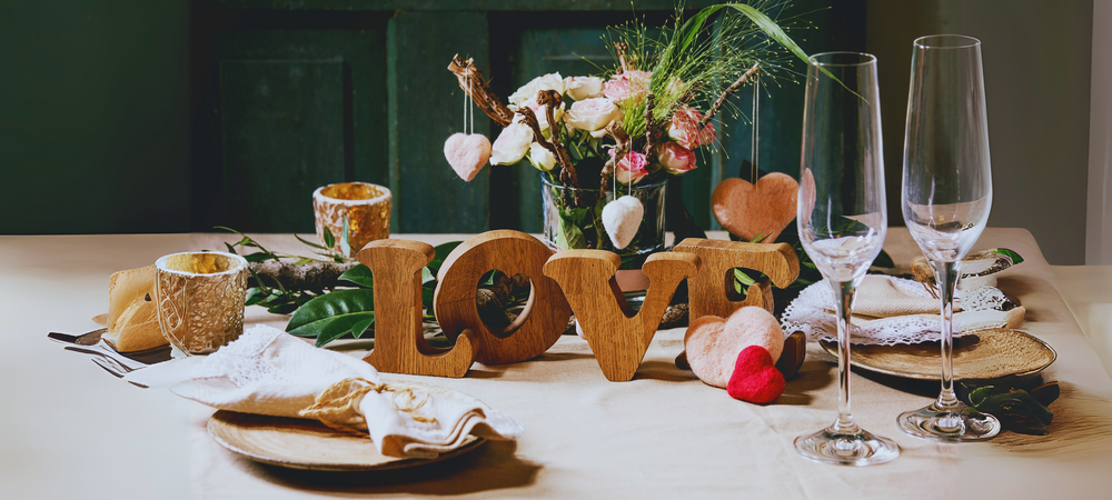 Valentinstag, gedeckter Tisch, Sektgläser und ein Schriftzug aus Holz "LOVE"