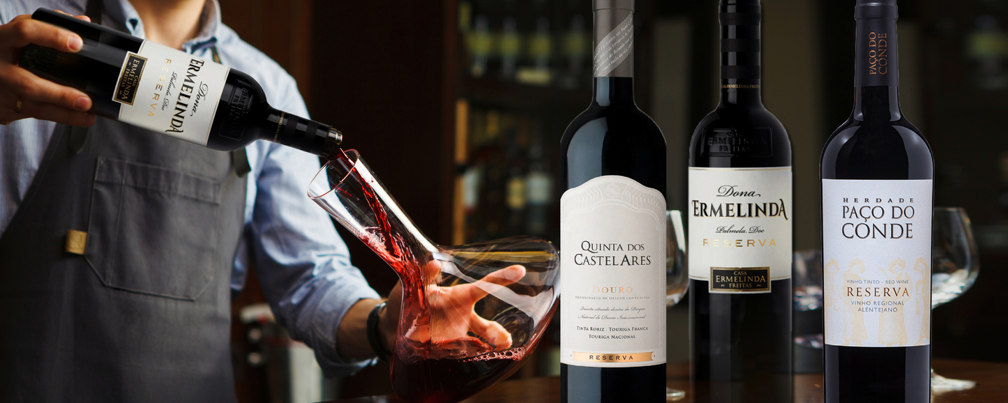 „Ein Sommelier dekantiert einen edlen roten Reserva in eine Glaskaraffe, daneben eine Auswahl portugiesischer Premium-Weine der Weingüter Dona Ermelinda, Quinta dos Castelares und Herdade Paço do Conde - erhätlich bei Vinho Bar.