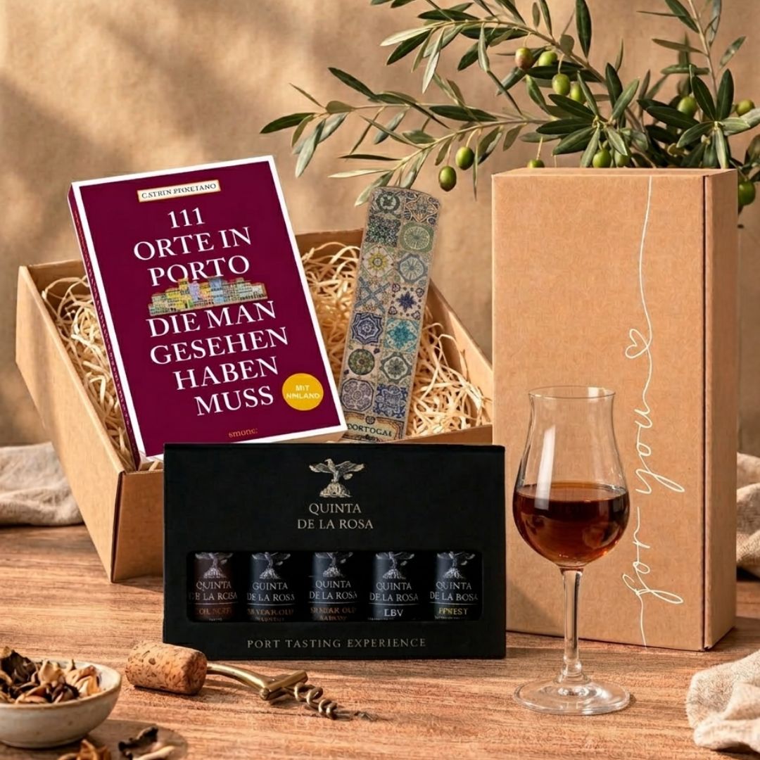 Ein Porto-Geschenkset auf hellem Untergrund. Im Fokus steht eine schwarze Box der „Quinta de la Rosa Port Tasting Experience“ mit fünf kleinen Portweinflaschen. Rechts daneben ist das Buch „111 Orte in Porto, die man gesehen haben muss“ von Catrin Ponciano platziert. Im Vordergrund liegt ein schmales Kork-Lesezeichen mit farbenfrohen, portugiesischen Azulejo-Mustern. Im Hintergrund ist ein brauner Kraftkarton mit der weißen Aufschrift „for you“ und einem kleinen Herz zu sehen.