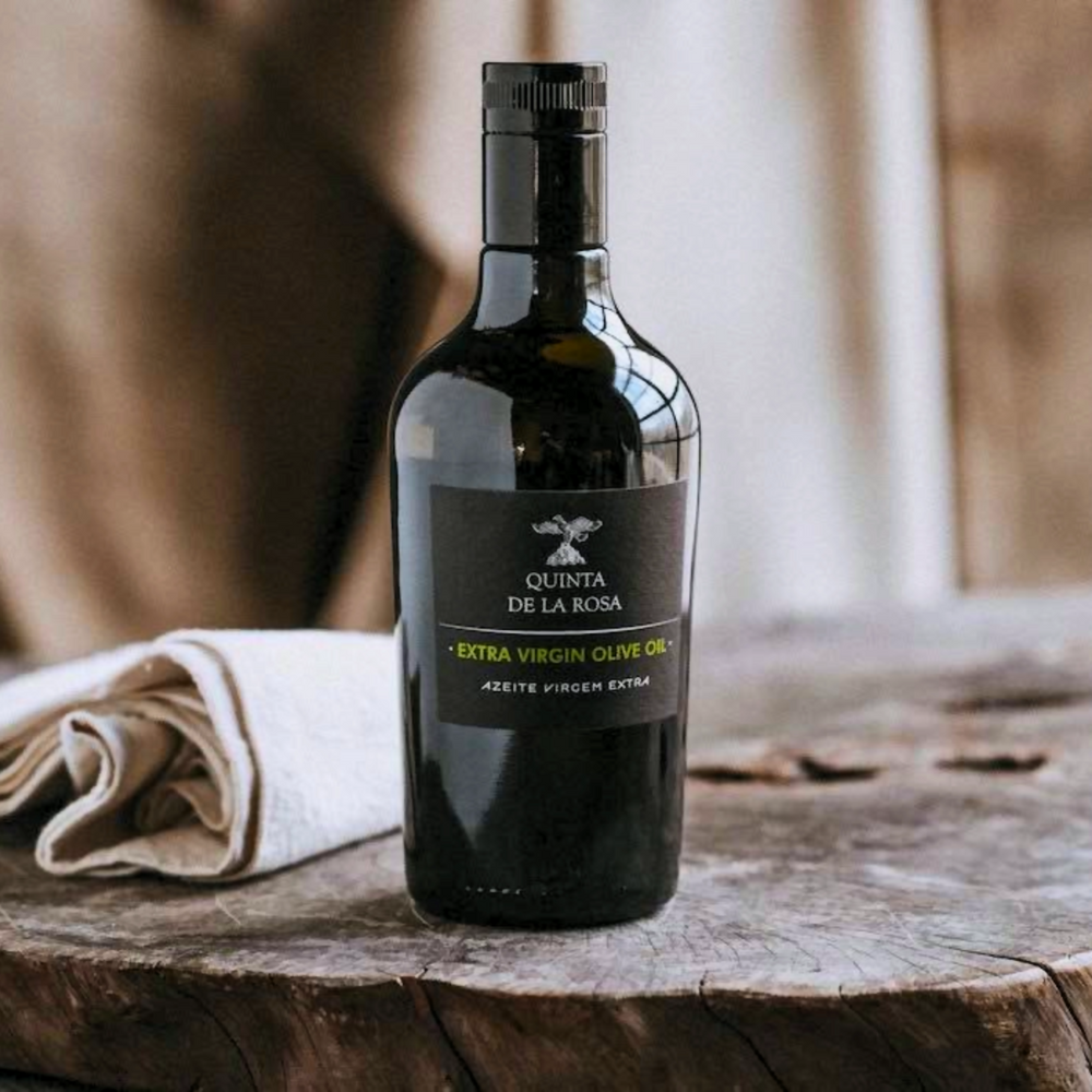 
                  
                    Flasche Olivenöl vom Weingut Quinta de la Rosa in Portugal. Die Flasche steht auf einer Holzscheibe eines Baumes, im Hintergrund ist ein beiges Tuch zu sehen.Erhältlich im Onlineshop der Vinho Bar.
                  
                