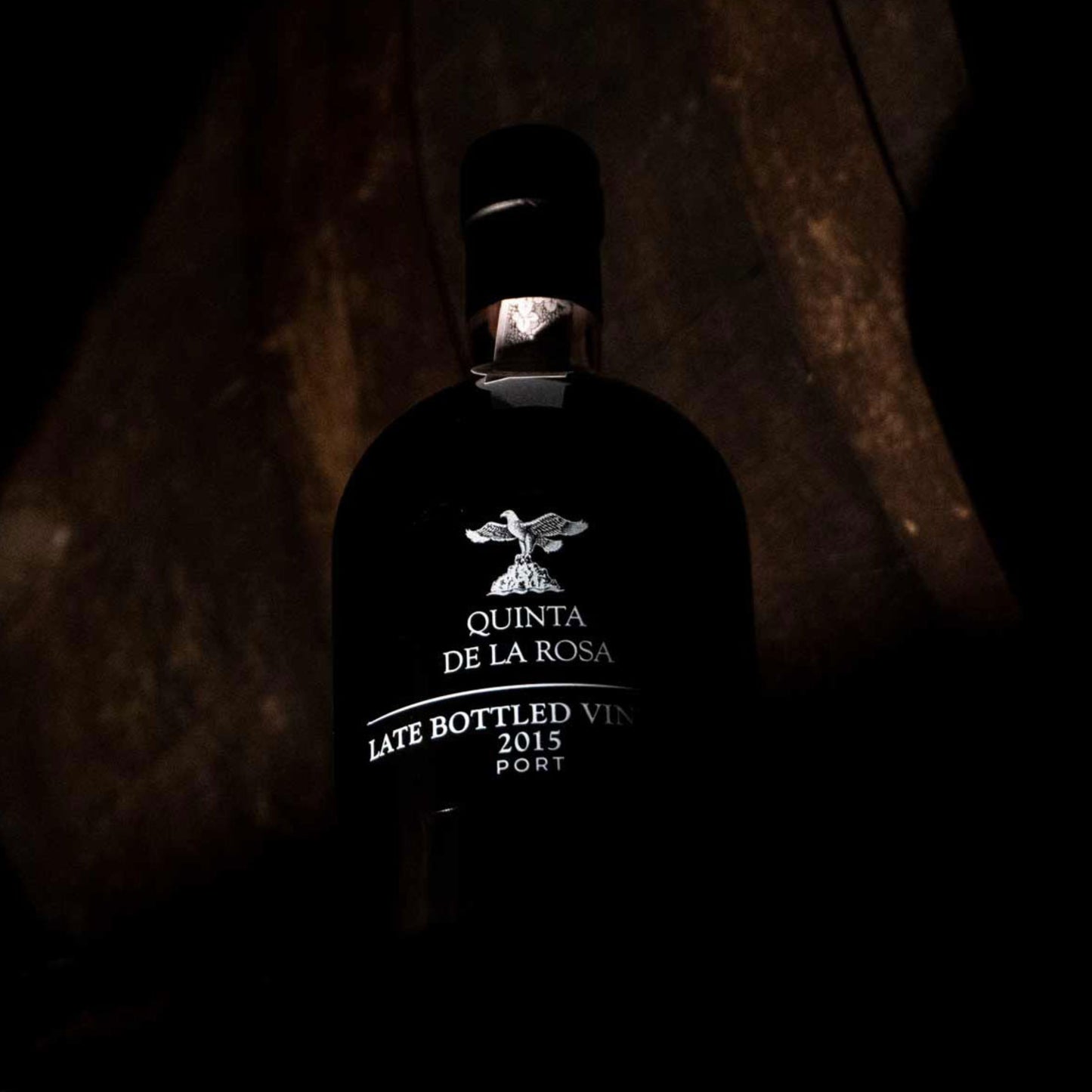 
                  
                    Dunkles, stimmungsvolles Foto einer Flasche Quinta de la Rosa Late Bottled Vintage Port 2015, die subtil beleuchtet ist und Eleganz und Tiefe des Weins hervorhebt.
                  
                