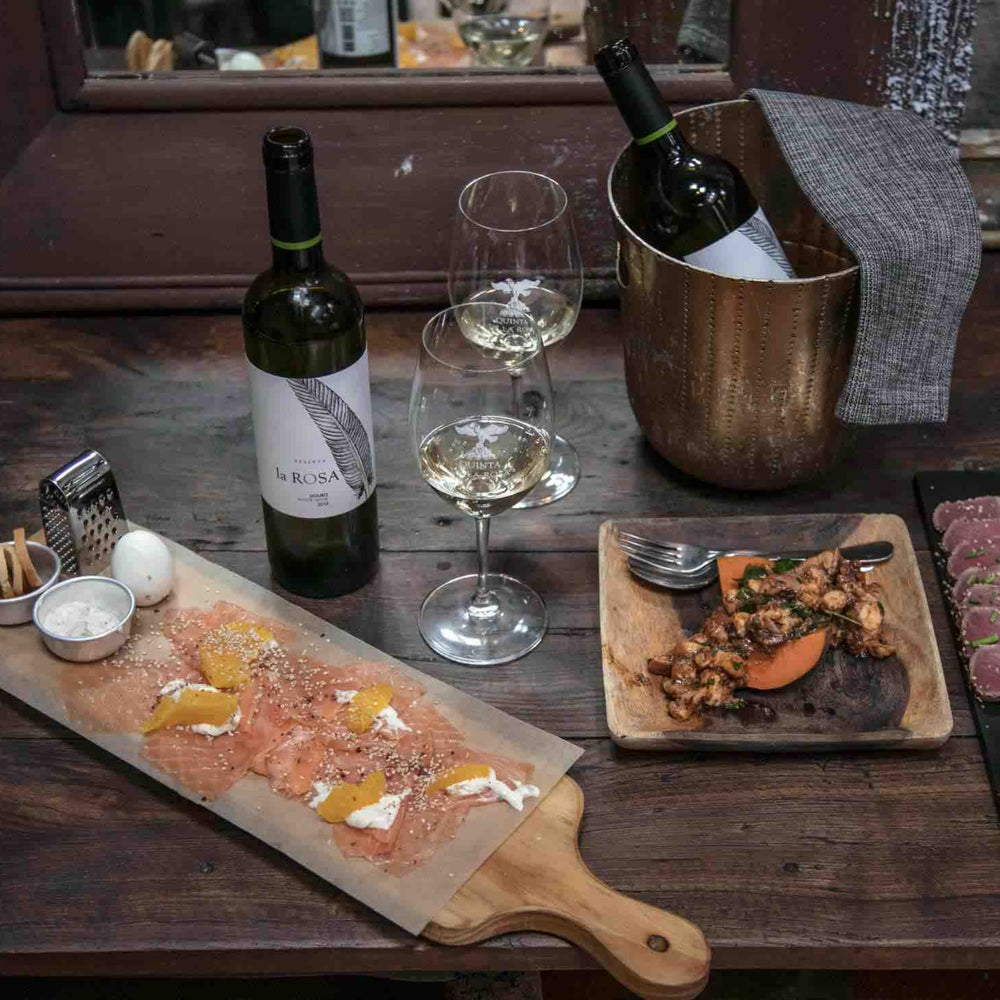 Flasche Quinta de la Rosa Weißwein Reserva auf einem Tisch mit Speisen und Weingläsern.