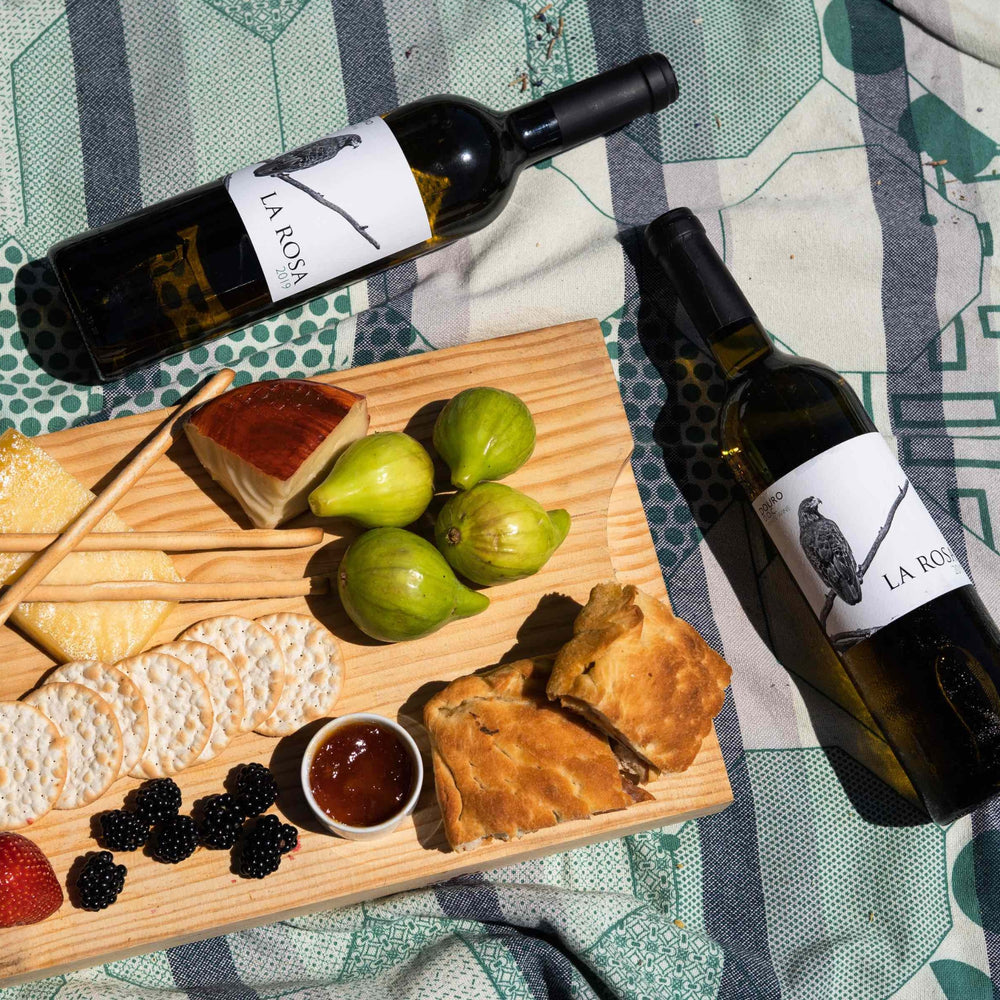 
                  
                    Flasche Weißwein vom Weingut Quinta de la Rosa, einem Weingut in Portugal. Zwei Flaschen liegen auf einer Decke, dazwischen ein Holzbrett mit Brot, Käse und Früchten.
                  
                