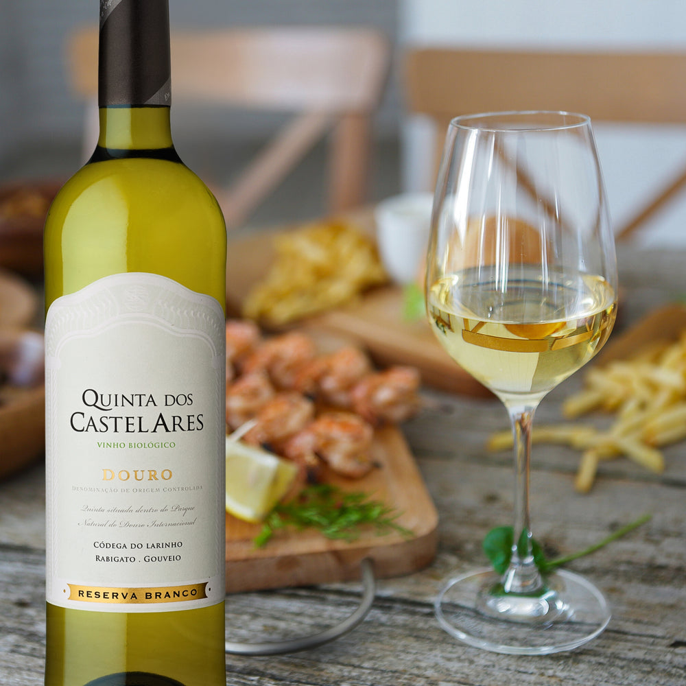
                  
                    Quinta dos Castelares,  Reserva Weißwein / Biowein aus dem Douro / Portugal.  Flasche mit gefülltem Weinglas, dahinter Speisen auf einem Holzbrett.
                  
                