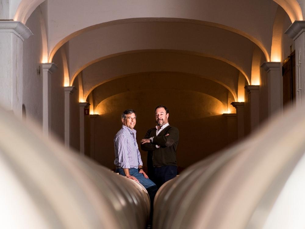 Luís und Carlos Mira auf Weinfässern sitzend im Weinkeller des Weingutes Herdade das Servas in Portugal.
