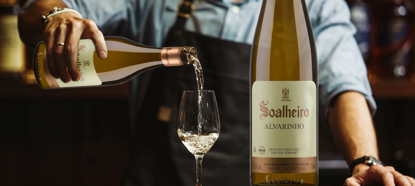 Im Bild sieht man einen Barkeeper, der Weißwein in mehrere Weingläser schüttet. Rechts im Bild ist eine Flasche Weißwein Alvarinho vom Weingut Soalheiro in Portugal. Weine erhältlich im Weinversand für Portugal Vinho Bar.