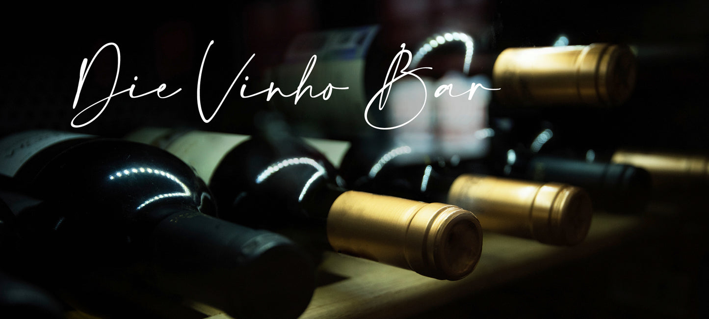 Foto mit einem alten Gebäude vor dem Weinfässer stehen, umgeben von Efeu. "Über uns Seite" der Vinho Bar aus Wuppertal - Portugiesischer Weinversand. Bild mit liegenden Weinflaschen.