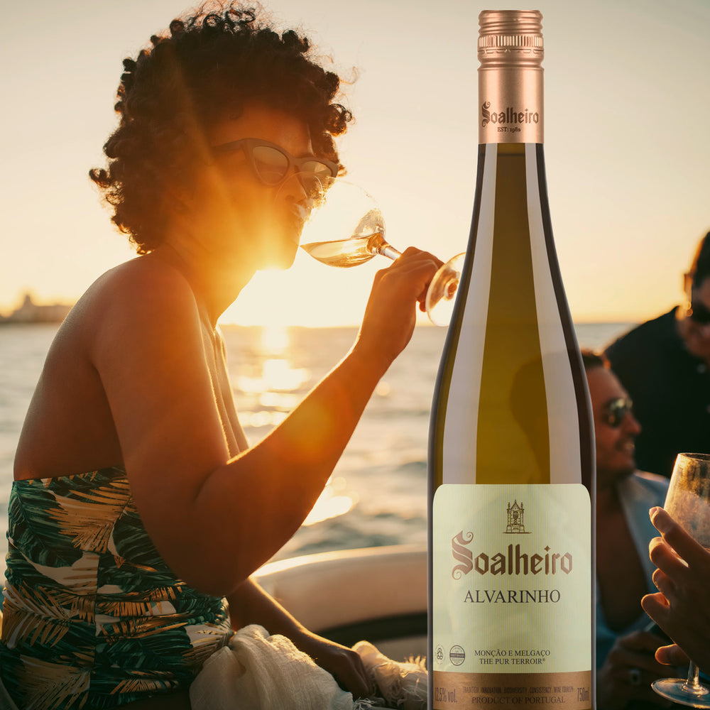 Das Foto zeigt eine Szene, in der eine Frau in einem Boot sitzt und Soalheiro Alvarinho Weißwein genießt. In der Nähe befinden sich weitere Personen, darunter Männer, die ebenfalls im Boot sitzen. Im Hintergrund erstreckt sich das ruhige Meer.