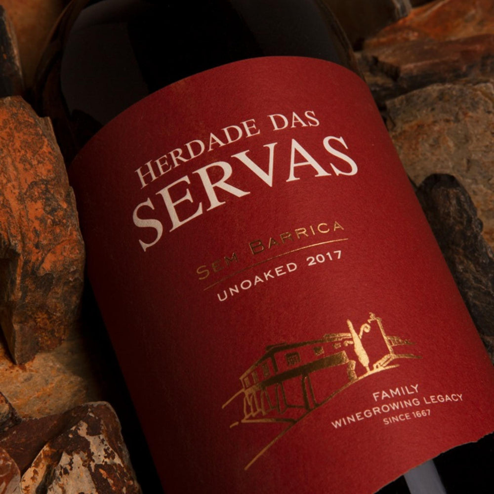 
                  
                    SEM BARRICA - UNOACKED Rotwein vom Weingut Herdade das Servas aus der Region Estremoz – Alentejo/Portugal. Flasche mit rotem Etikett zwischen Steinen liegend.
                  
                