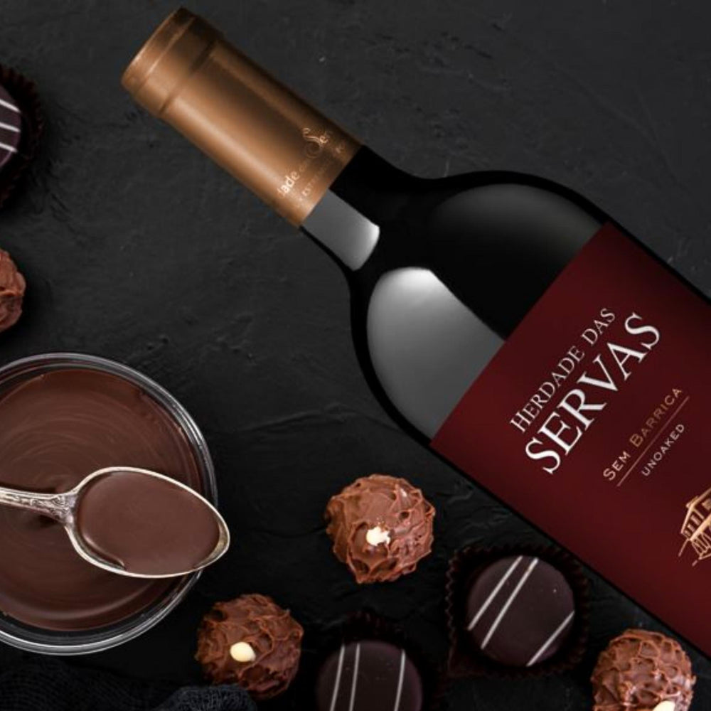 
                  
                    SEM BARRICA - UNOACKED Rotwein vom Weingut Herdade das Servas aus der Region Estremoz – Alentejo/Portugal. Flasche auf Schieferplatte liegend, daneben Schokoladenpralinen und eine Schüssel mit flüssiger Schokolade und einem Löffel.
                  
                