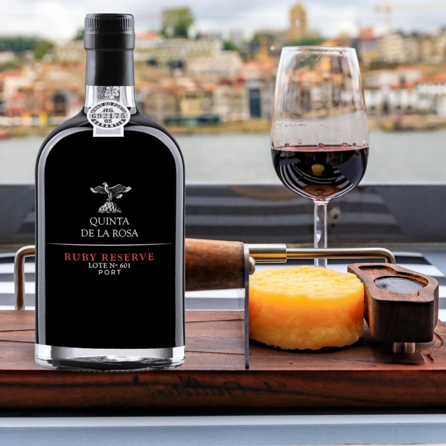 
                  
                    Ruby Reserve, Portwein vom Weingut Quinta de la Rosa. Bild am Douro mit Landschaft im Hintergrund und einem Portweinglas mit Käse daneben.
                  
                