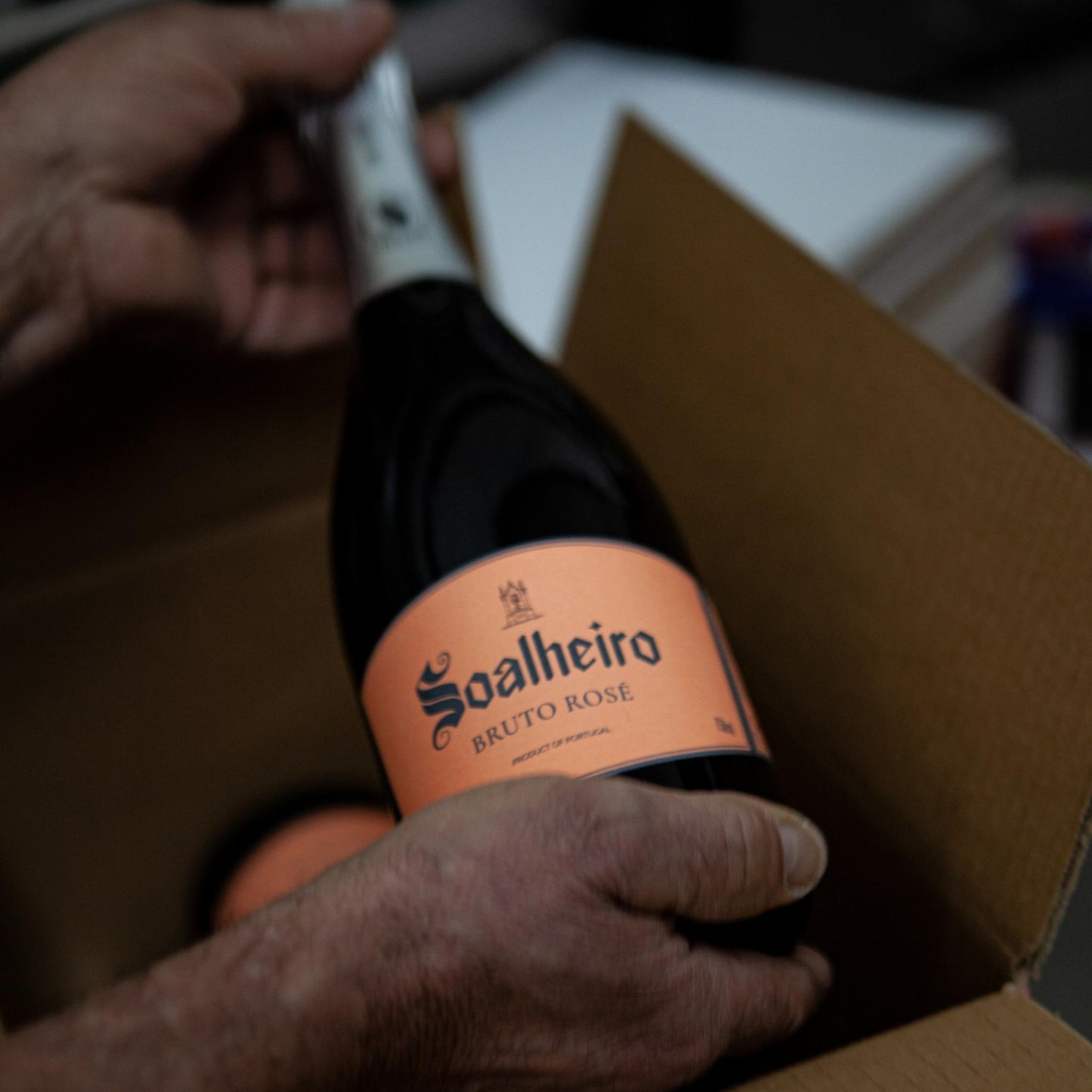 
                  
                    Eine Flasche Rosé Schaumwein / Sektflasche vom Weingut Quinta da Soalheiro aus der Region Vinho Verde, Minho IGP / Portugal. Erhältlich im Portugalweinversand VINHO BAR in Wuppertal. Ein Mann hält die Flasche Sekt in den Händen und packt sie in einen Karton.
                  
                