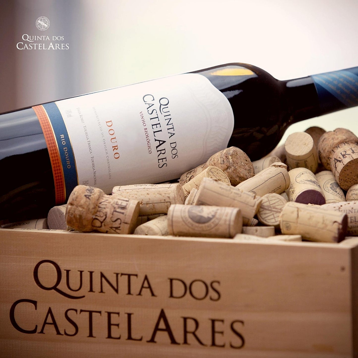 
                  
                    Quinta dos Castelares Colheita Rotwein, Biowein aus dem Douro / Portugal. Bild mit der Weinflasche liegend in einer Holzkiste mit Logo des Weingutes mit Weinkorken gefüllt.
                  
                