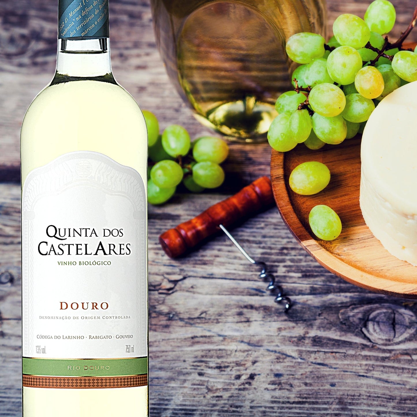 Quinta dos Castelares Colheita Weißwein aus dem Douro / Portugal. Biowein.  Im Hintergrund auf dem Bild: Käse, und Weintrauben auf  einem Holzteller und ein Korkenzieher.